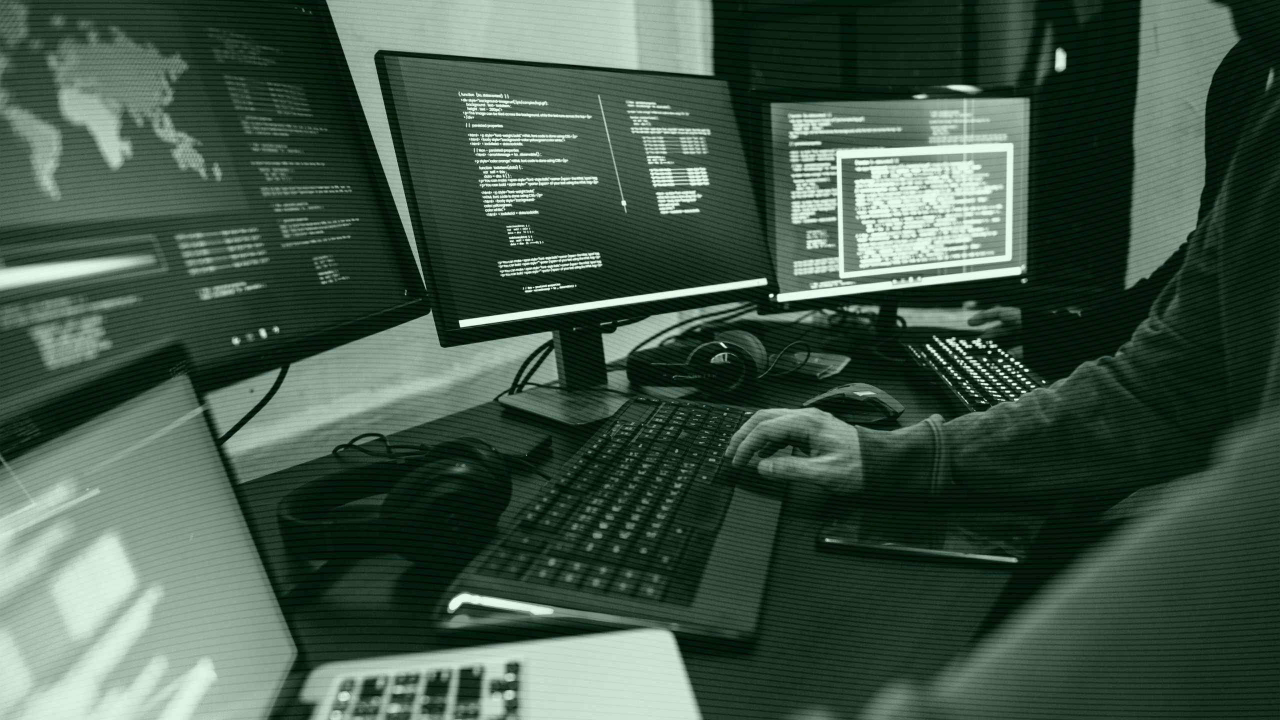 Photo of a hacker looking at code on several monitors