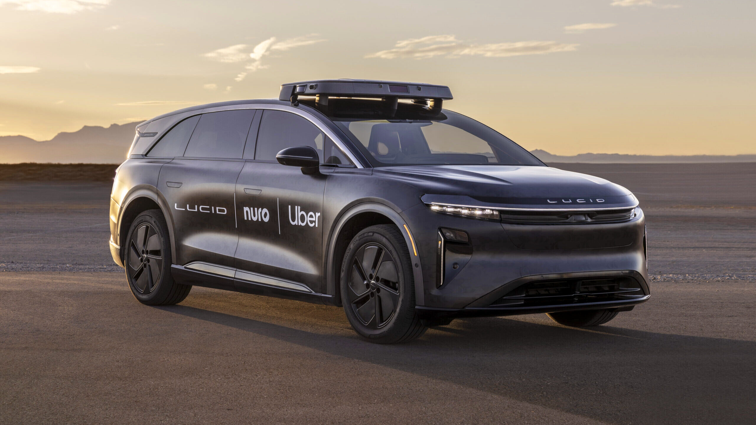 A black Lucid electric vehicle is shown with the logo of the company, as well as the logos of Uber and Nuro, painted in white lettering on its side.