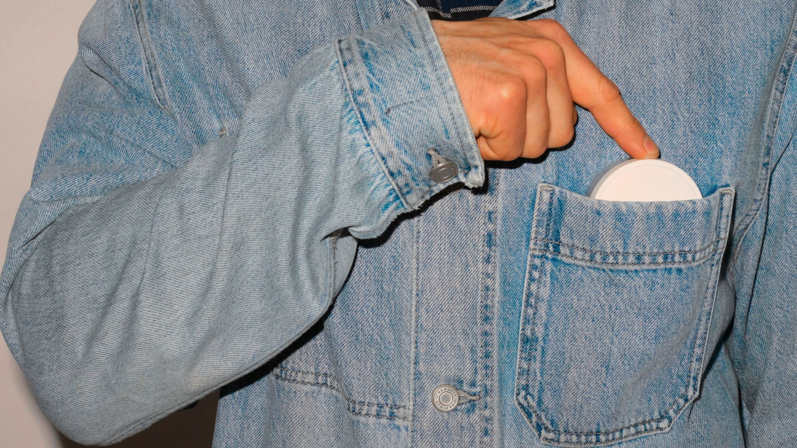 A person is shown placing a nicotine pouch container in the breast pocket of their jean jacket.