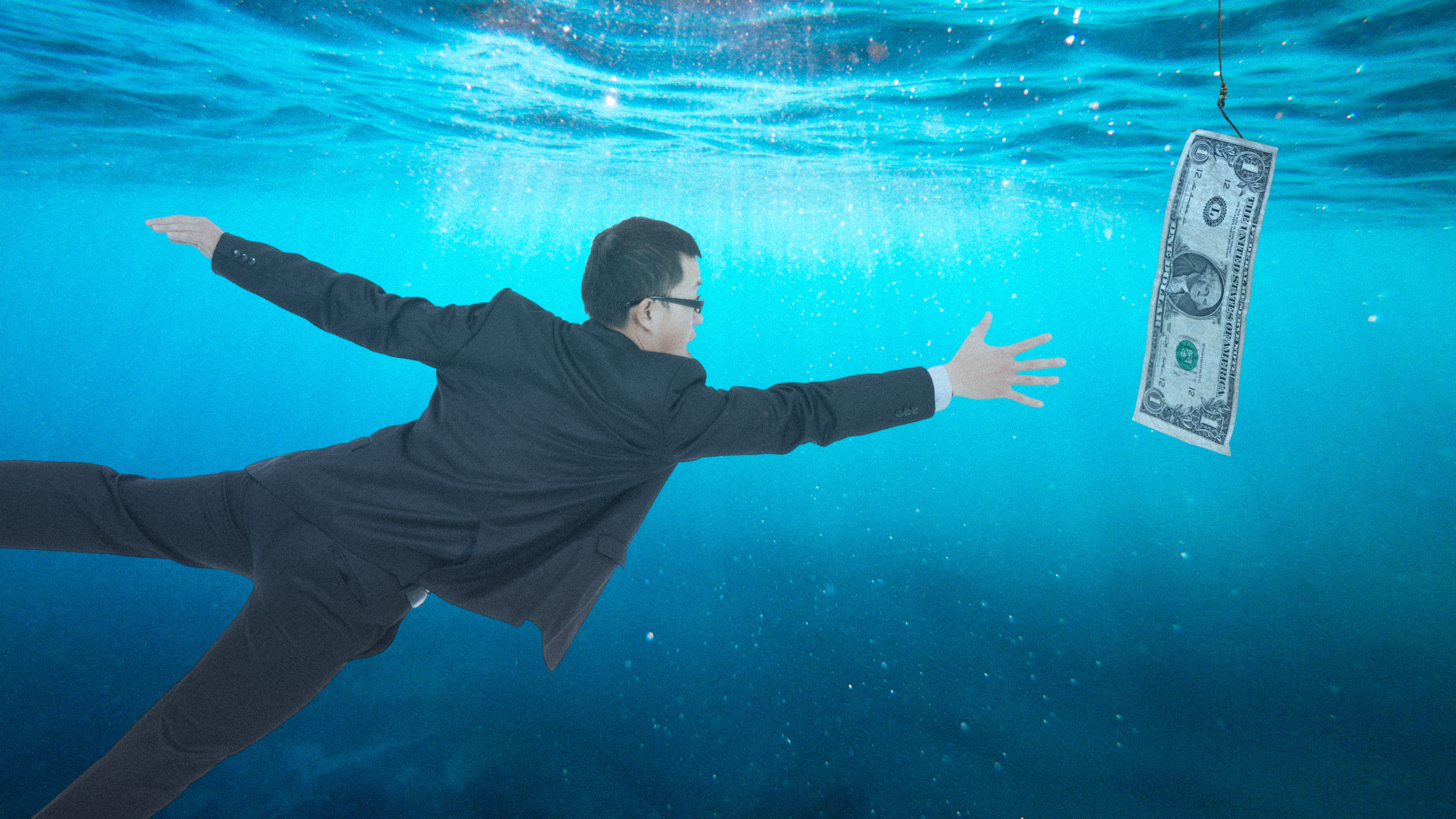 Photo illustration of a man in a suit reaching for a one dollar bill underwater