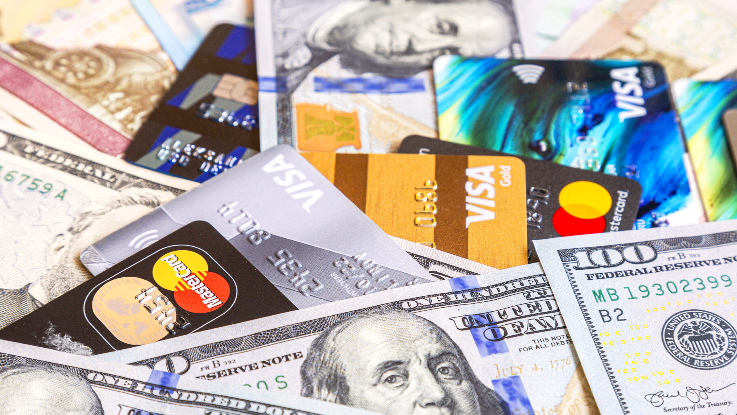 Several Visa and Mastercard credit cards are shown overlapping on a table along with US $100 bills.