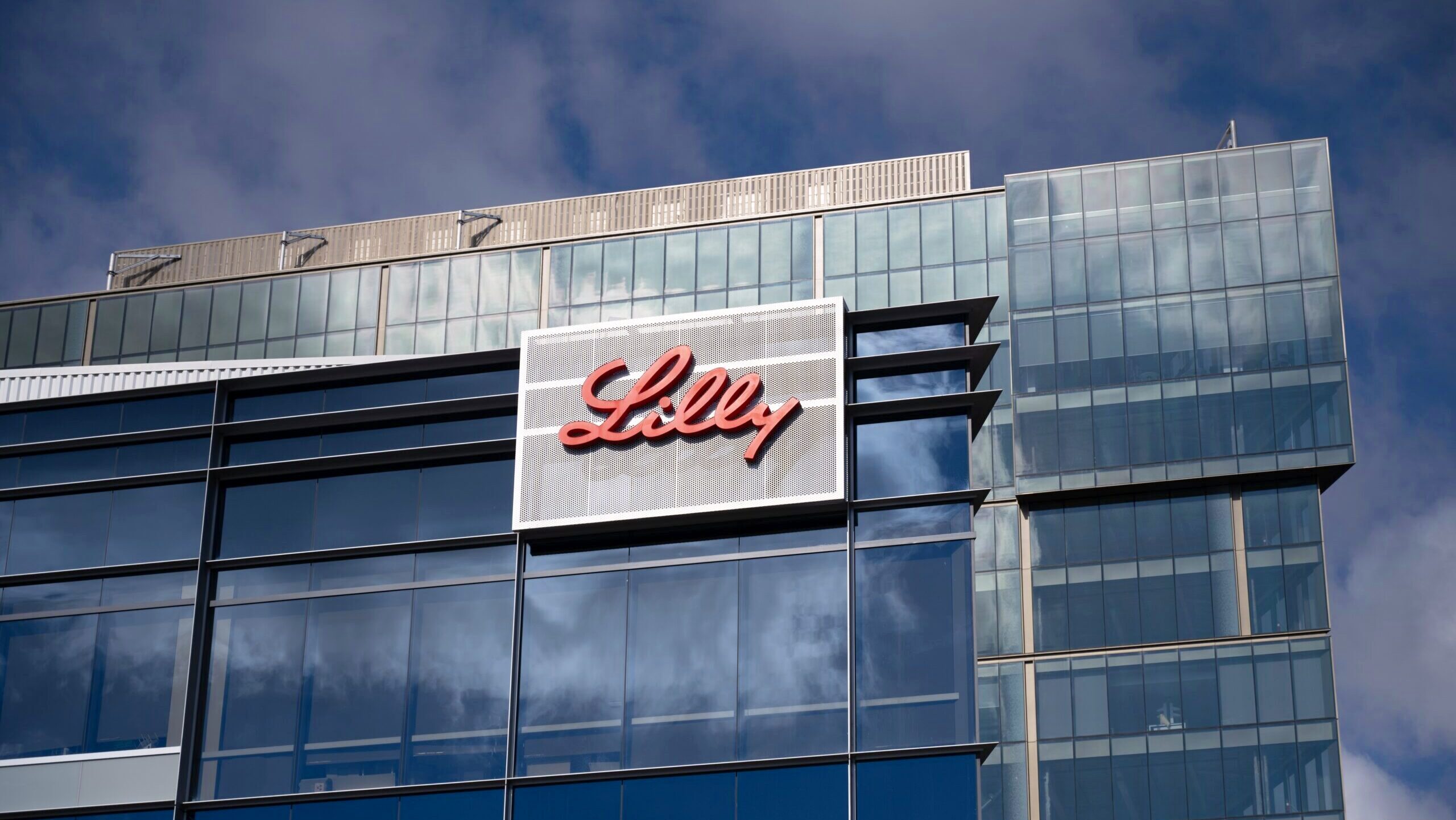 The Eli Lilly logo is shown on a glass office building facade.