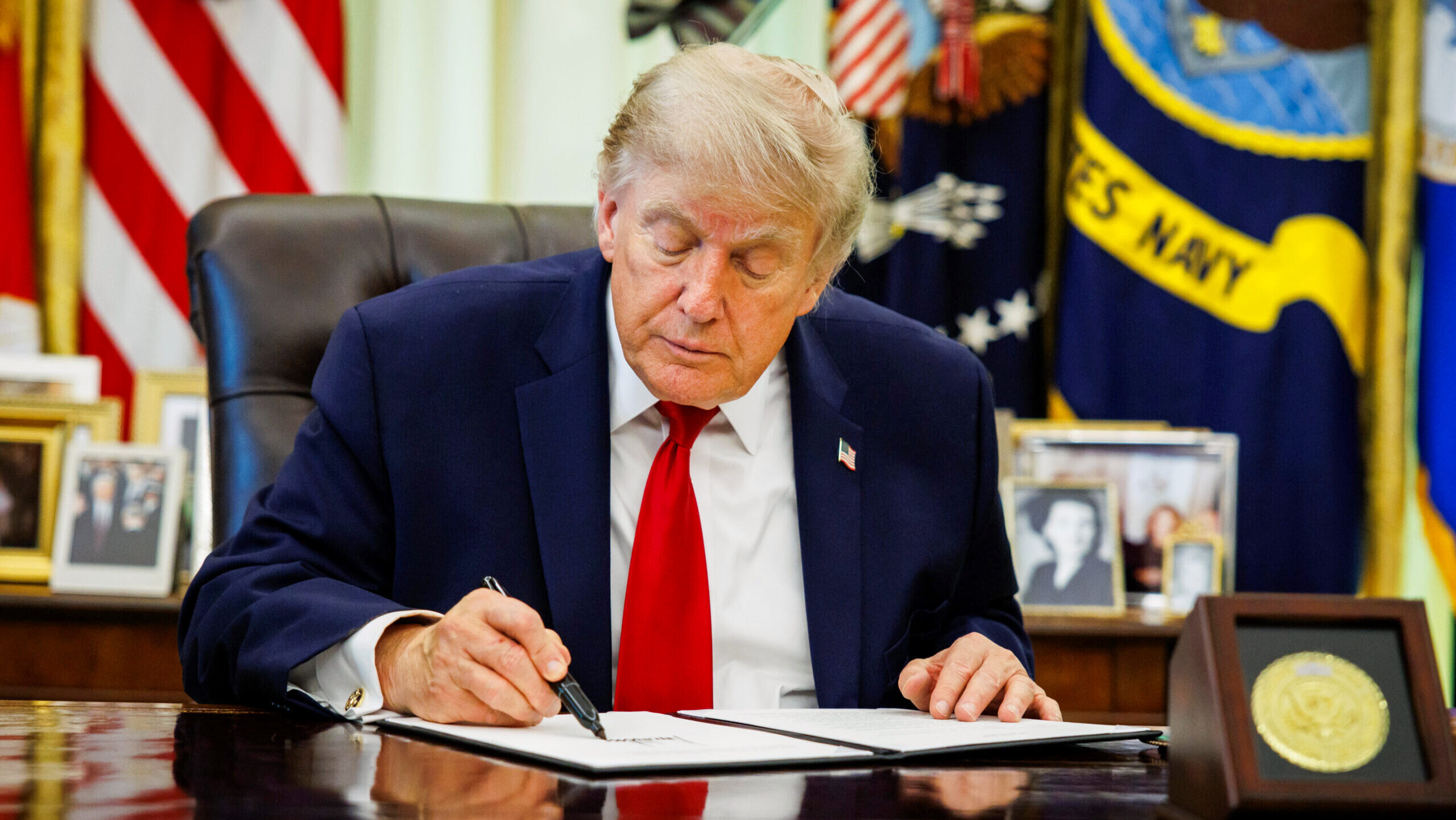 Photo of US President Donald Trump signing a document at the Resoulute Desk in the Oval Office.